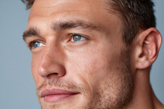 Close up of male face with textured skin, defined jawline and blue eyes showing contemplative expression and natural stubble