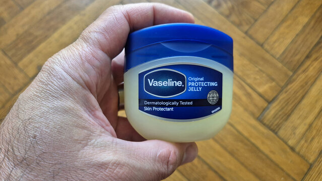 A hand holding a tub of Vaseline Original Protecting Jelly against a wooden parquet background. Picture taken on April 26, 2026 in Bucharest, Romania.
