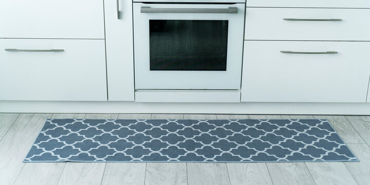 Modern kitchen design featuring sleek white cabinetry, a built in oven, and decorative grey moroccan trellis floor mat