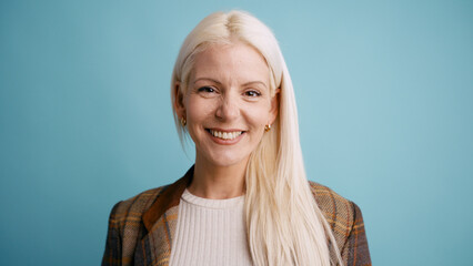 Blonde woman with a natural smile looking directly at the camera, conveying happiness and positive emotion against a blue backdrop © DMegias