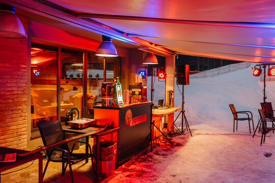 Outdoor bar area with illuminated counter and seating under a canopy, snow-covered landscape visible in the background