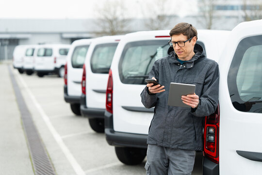 Fleet manager with digital tablet and smartphone supervising rows of white delivery vans