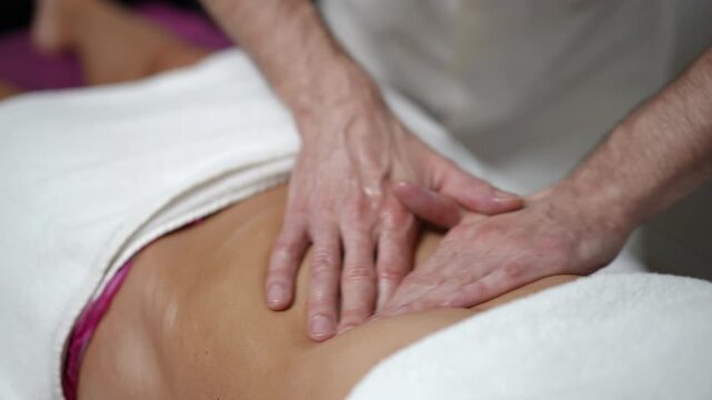 Close-up shot of a professional male masseur applying oil and giving a deep visceral massage on a woman's belly in a spa clinic