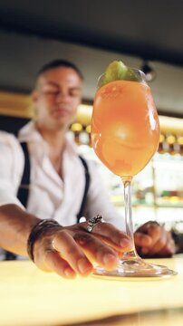 Slow motion of a professional bartender sliding a delicious orange cocktail on a bar counter. An elegant mixologist serving an aperitif