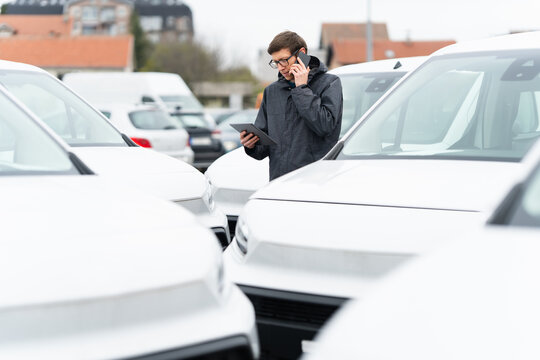 Fleet manager with digital tablet and smartphone supervising rows of white delivery vans