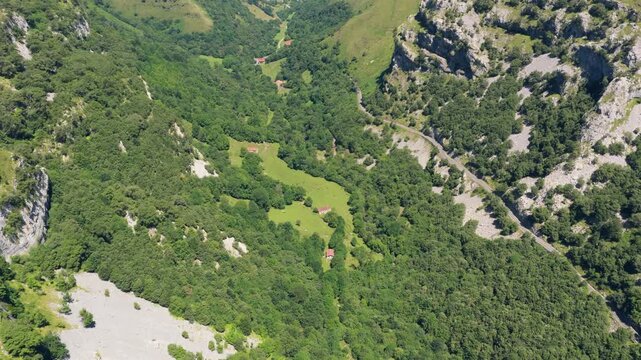 High angle shot of a stunning mountain valley in summer. Lush green forests and pastures dot the landscape, with a few rustic farmhouses scattered throughout