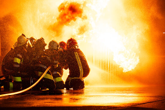 Silhouette of firefighters training for disaster relief officers.Firefighter using water and fire extinguishers to fight the flames in emergency situations in a dangerous area fire site on night time.
