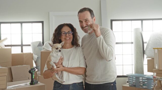 Man and woman kiss holding a small dog and house keys surrounded by moving boxes in building; new home joy.