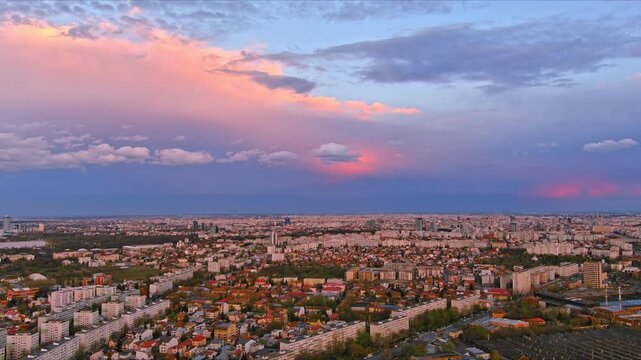 Bucharest, Romania - 15 April 2026: Aerial view of the sprawling urban landscape of Bucharest with residential blocks and green spaces under a dramatic pink and blue sunset sky.