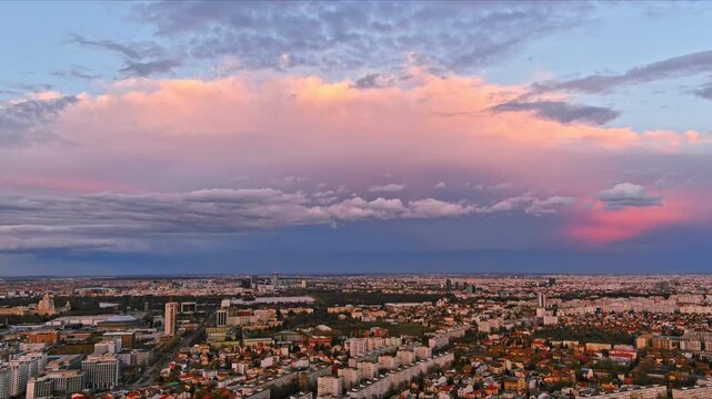 Bucharest, Romania - 15 April 2026: Aerial view of the city skyline with residential buildings and green areas under a dramatic sunset sky with pink clouds.