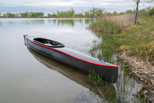 decked touring canoe with carbon fiber hull and rudder at a shore of calm lake