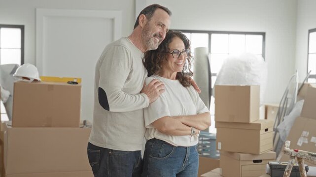 Man standing beside moving boxes with hand on woman's shoulder in a light filled building; new home contentment.
