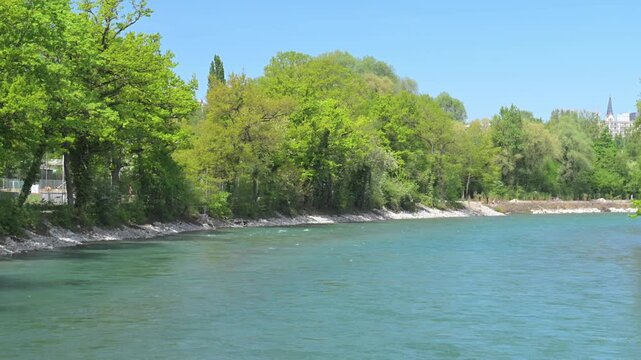 Calm river water flowing past green woodland under clear blue sky in Bern, Switzerland.