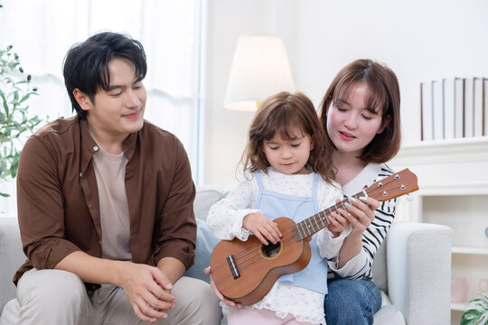 A child enjoys playing a ukulele with their parrent