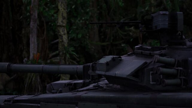 Idle tank after jungle training exercise, hull coated with grime and mud, passive posture beside tree line, postoperation atmosphere with worn metal and quiet