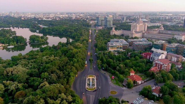 Bucharest, Romania - 27 August 2020: Aerial view of the House of the Free Press and Herastrau Park with lush green trees and a lake at sunset.