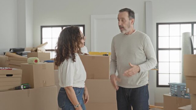 Man and woman arguing, woman pointing finger at packed cardboard boxes during moving in building; frustration planning.