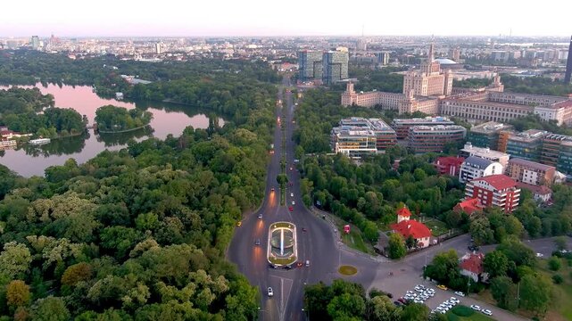 Bucharest, Romania - 27 August 2020: Aerial view of the House of the Free Press and Herastrau Park with lush green trees and a lake at sunset in Bucharest.