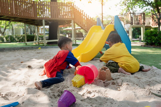 Asian boy playing with toy truck in outdoor sandbox.