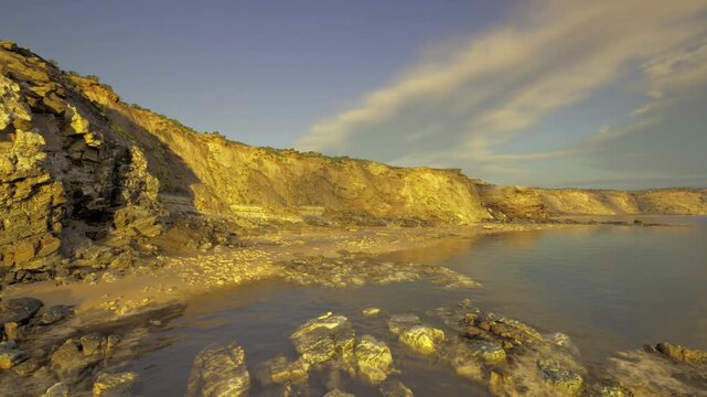wide rugged cliff coastline under streaked clouds and warm light, tide pools in foreground and strong rock texture, cinematic atmosphere for exploration imagery