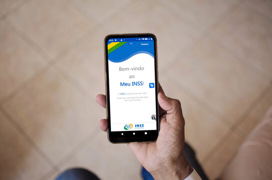 National Institute of Social Security (INSS). Woman holding a smartphone with the Meu INSS app on the screen, checking her benefits. 