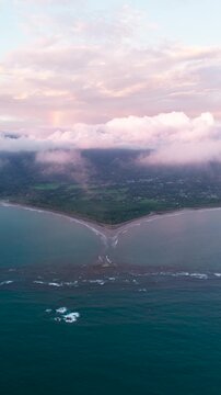 Stunning aerial perspective of the iconic whale tail shaped tombolo at Uvita, Costa Rica, with a beautiful sunset and a faint rainbow. Vertical
