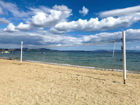 Empty beach volleyball net on a sandy shore, Attica Greece. Seaside court, calm Aegean sea water, blue sky