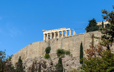 Fototapeta premium Parthenon temple on the Acropolis hill in Athens, Greece. Stone walls and green trees, blue sky, sunny day