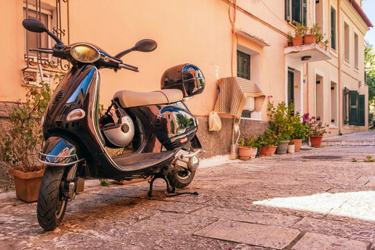 Black scooter parked on narrow Mediterranean street with pastel buildings in Corfu island old town, Greece