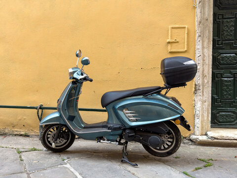 Blue scooter parked beside yellow wall and green door in old town street of Corfu island Greece
