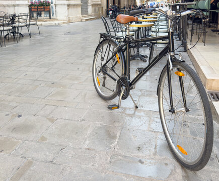 Black city bicycle parked near outdoor cafe tables on sunny morning in Corfu Greece old town street