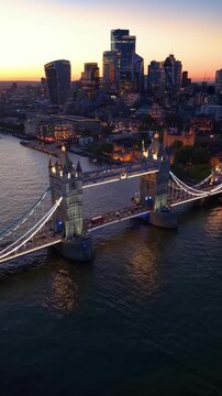 Establishing aerial view of the famous Tower Bridge and the illuminated skyline of London, England, during dusk