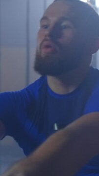 Focused athletic man intensely training on cardio rowing machine during challenging workout session in dimly lit gym environment, expressing effort and endurance