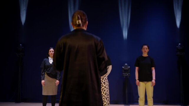 Vocal ensemble rehearsal on theater stage with passionate conductor leading singers under dramatic spotlights during intimate musical performance