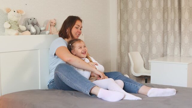 A loving moment of reading between a mother and child in a bright, soft bedroom. Early literacy and learning. Wide shot