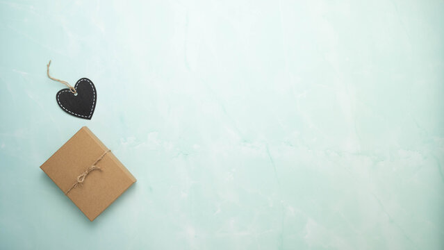 Brown paper gift box with a black chalkboard heart shaped tag on a blue and white marbled surface.