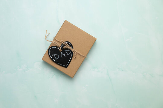 Brown paper gift box with a black chalkboard heart shaped tag on a blue and white marbled surface.  Father's day, birthday background.