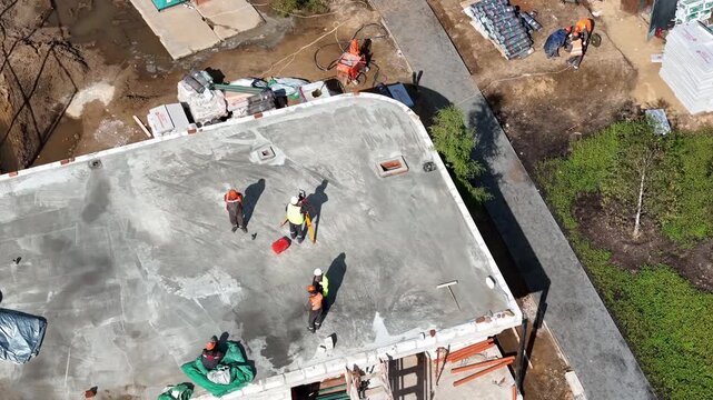 Workers build concrete roof. Team moves materials across roof. Greenery surrounds construction site. Sky views show progress. Ideal for construction projects. Workers focused, moving quickly