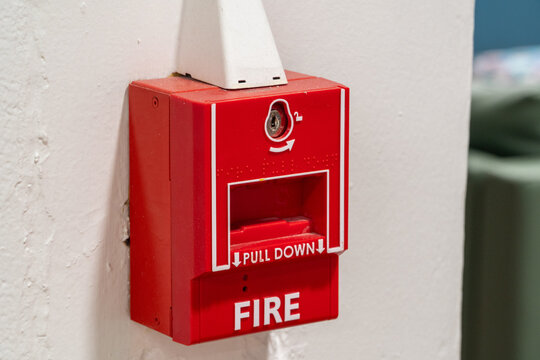 Red manual fire alarm pull station mounted on a textured white wall, essential for immediate emergency notification and building safety protocols, awaiting activation during a fire event.