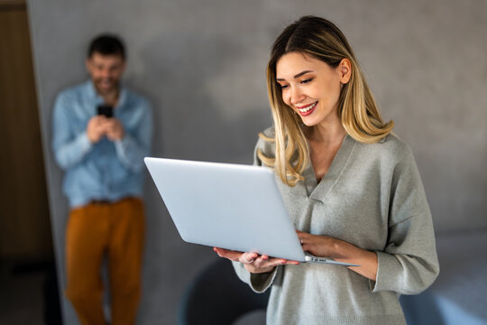 Young happy multiethnic couple having fun while using laptop, digital device at home