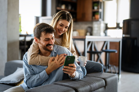 Smiling young couple embracing while looking at smartphone. Multiethnic couple sharing social media