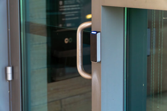 Modern glass door with an illuminated RFID card reader and metal handle for secure automatic entry to contemporary office buildings or facilities, symbolizing controlled access and technology.