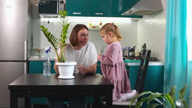 Mother and daughter enjoying plant care at home, checking leaves and soil, learning responsibility, eco habits and positive parenting indoors.