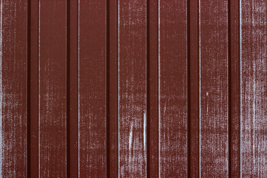 Vertical brown corrugated metal siding with weathered scratches and paint wear.