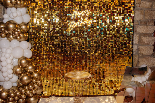 A luxurious birthday photo zone features a shimmering gold sequin backdrop with a neon sign, chrome and white balloon garland, golden pedestal table and mirror number decor