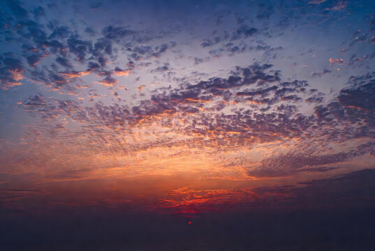 A vibrant sunset with scattered clouds over a body of water.