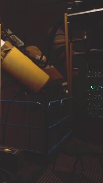 A cart stands in a storage room filled with various items. Boxes and furniture pieces are stacked haphazardly. The low light creates shadows in the space, showing disorganization.