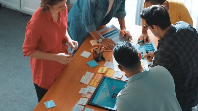 Top view of manager writing idea on sticky notes and explain idea about web design. Professional marketing team or programmer brainstorming idea while looking at tablet with color palette. Symposium.
