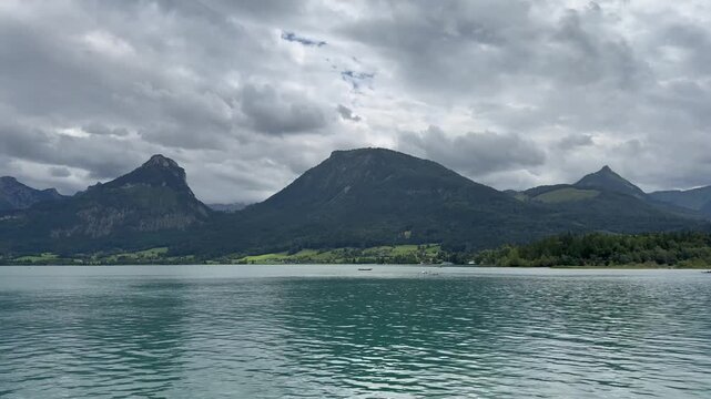 Panoramic, scenic view of Wolfgangsee Lake. Tiny rowing boats move across the lake. Motion of lake waves. Wolfgangsee, Austria