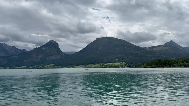 Panoramic, scenic view of Wolfgangsee Lake. Tiny rowing boats move across the lake. Motion of lake waves. Wolfgangsee, Austria